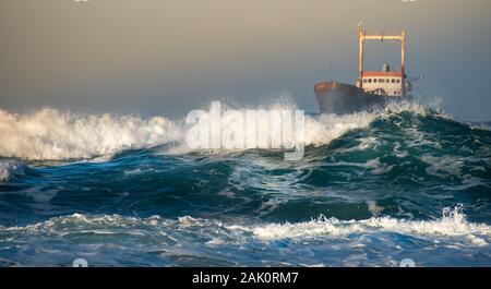 Abandoned ship in the stormy sea with big wind waves during sunset. Stock Photo