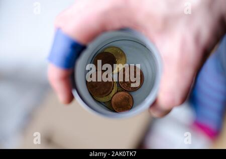 A person holding a cup with some coins begging for more change. Stock Photo