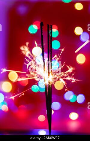 Glittering burning sparkler on red and color bukeh  background Stock Photo
