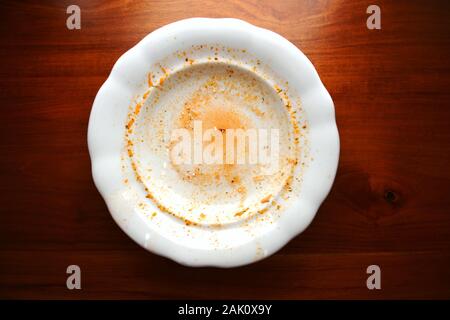 Empty white porcelain plate with finished food leftovers from soup or sauce lays on wooden table, flat lay top view Stock Photo