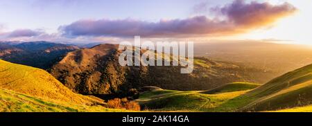 Panoramic sunset view of hills and valleys in the Diablo mountain range starting to turn green; San Jose and bright light from the setting sun visible Stock Photo