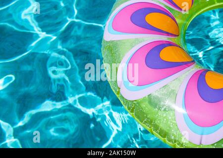 Brightly colored pool ring floating on dappled turquoise water in tropical sun Stock Photo