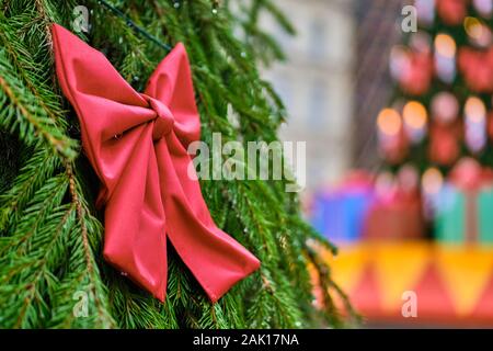Christmas decoration in the form of a red bow with a yellow ball against the background of a blurred tree with lights. Close up. Stock Photo