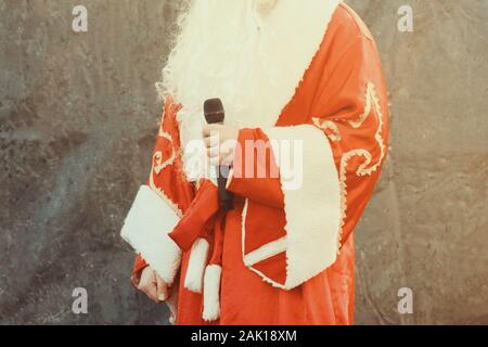 The actor dressed as Santa Claus performs on stage with a microphone against a black background. Close up. Stock Photo