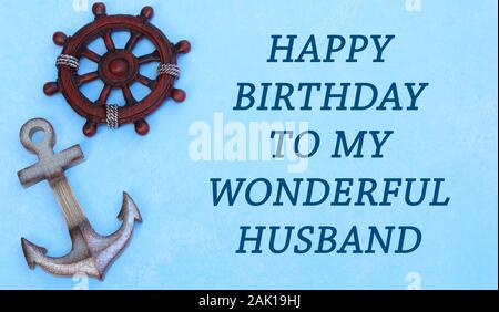 ship anchor and wheel laying on a blue background with happy birthday to my wonderful husband in blue text Stock Photo