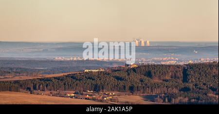landscape - forest and hill with church in the foreground, city in the background and nuclear power plant chimneys (Temelin, Czechia) on the horizon Stock Photo