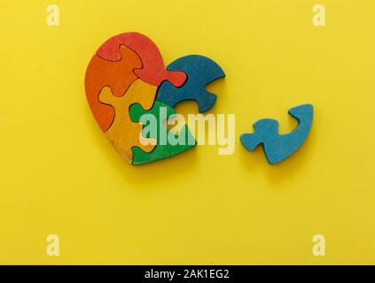 Wooden multicolor puzzle in the form of heart on yellow background. Concept valentines day, relationship. Stock Photo