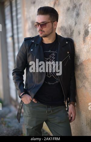 Young Man with sunglasses in a jacket standing by a wall. Stock Photo