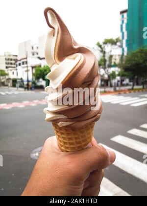 Ice cream cone held by a hand in the street of some city Stock Photo