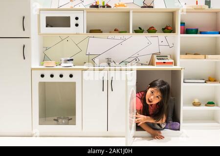 Beautiful girl coming out of the kitchen cupboard for girls Stock Photo