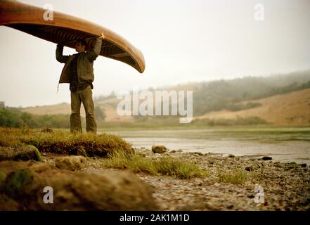 Man carrying canoe beside lake Stock Photo