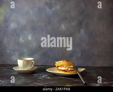 A cup of black coffee next to a plate with two cinnamon rolls in icing and a fork. Close-up. Stock Photo