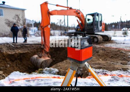 A selective focus view of a blurry excavator digging a hole on a construction site. ready for installation of septic tanks with laser level in front Stock Photo
