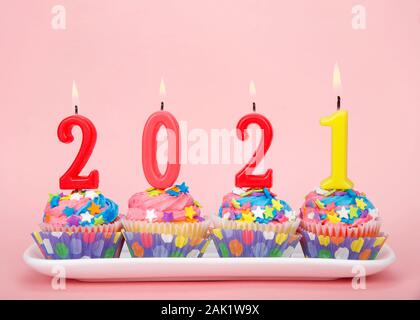 White cupcakes with rainbow colored frosting and brightly colored star candies on a rectangular plate pink background with 2021 candles burning. Happy Stock Photo