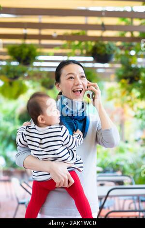 Woman talking on smartphone with holding baby Stock Photo