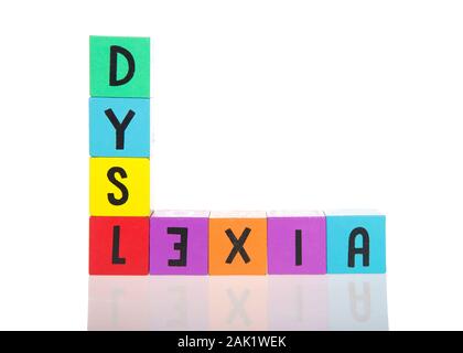 Bright colorful wooden toy blocks stacked on a reflective surface spelling dyslexia. Learning challenges disabilities. E is backwards. Isolated on whi Stock Photo