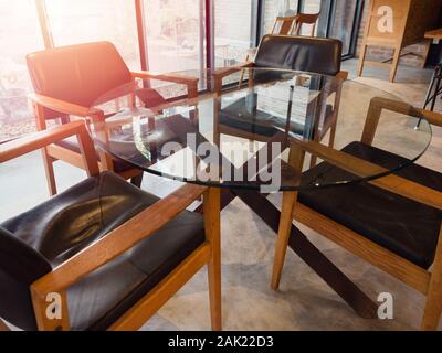 Modern round glass table with four wooden chairs in living room loft style near window glass with sunlight from outside. Stock Photo