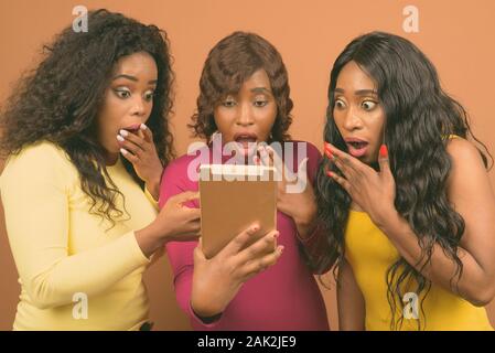 Young beautiful African twin sisters and friend against brown background Stock Photo