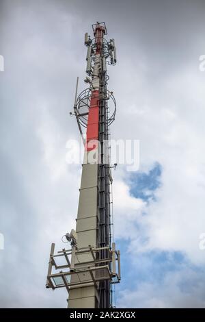 View of a tower with telecommunications antennas, concrete pole structure and equipments, cloudy sky as background Stock Photo