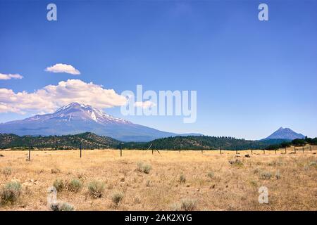Mount Shasta with snow and icecap in summer is an enormous volcano in California. It towers above the surrounding plains and hills. Stock Photo