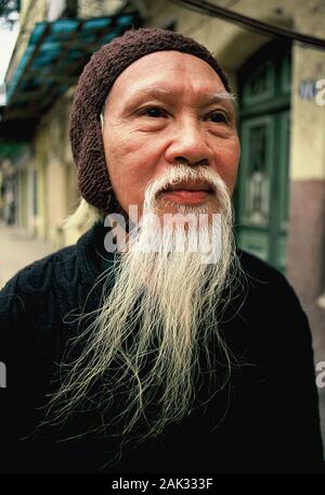 An old Vietnamese with a long beard walking through a street in Hanoi, that is the capital of Vietnam and is located in the north of the Southeast Asi Stock Photo