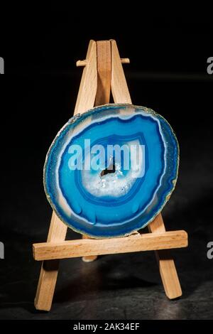 Studio shot of a round, thin, polished and blue-banded agate disc with druse (hole in the middle part) standing dripping wet on a miniature easel in t Stock Photo