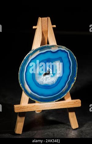Studio shot of a round, thin polished and blue banded agate slice with druse (hole in the middle part) standing in the front light on a miniature ease Stock Photo