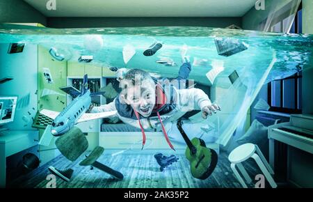 6 year old caucasian child plays happy with an airplane in his flooded room. Surreal image, concept of light-heartedness. Stock Photo