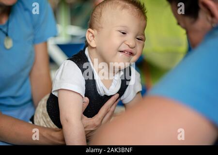 Portrait of a baby with cerebral palsy on physiotherapy in children therapy center. Boy with disability has therapy by doing exercises. Special needs. Stock Photo