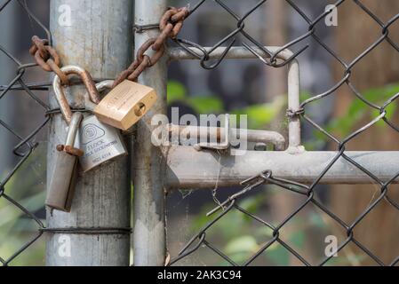 A steel and chain wire gate and gate post with three padlocks and a chain securing the entrance Stock Photo