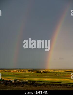 East Lothian, Scotland, United Kingdom, 7th January 2020. UK Weather:  A yellow warning is in place until 9pm tonight with gusts up to 80mph expected. A very brief appearance of the sun lit up a double rainbow looking North towards the Firth of Forth across the agricultural landscape Stock Photo