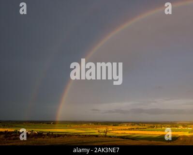 East Lothian, Scotland, United Kingdom, 7th January 2020. UK Weather:  A yellow warning is in place until 9pm tonight with gusts up to 80mph expected. A very brief appearance of the sun lit up a double rainbow looking North towards the Firth of Forth across the agricultural landscape Stock Photo