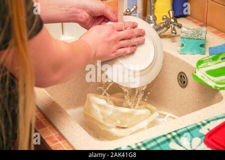 A woman washes dishes in the sink in her home kitchen Stock Photo