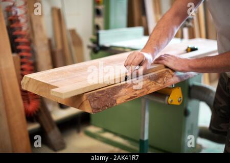 Carpenter or woodworker measuring a block of wood marking it off with a marker on a workbench in a woodworking workshop Stock Photo