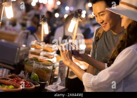 Happy young Chinese couple taking photos with smartphone in street market Stock Photo