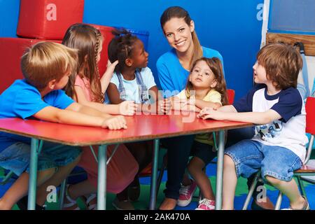 Happy group of kids sits with a smiling educator in kindergarten at the table Stock Photo