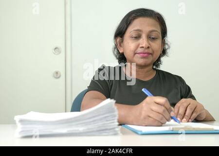 Woman manager or executive going through documents in a file and writing on paper. Office setting. Stock Photo