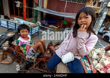 Poor girls whose homeless family scavenges for recyclable material sit on a motorcycle in front of their makeshift shelter in Kampong Cham, Cambodia. Stock Photo