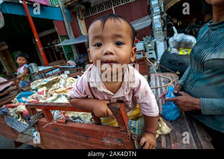 A poor toddler whose homeless family scavenges for recyclable material sits a vehicle used to transport recyclables in Kampong Cham, Cambodia. Stock Photo