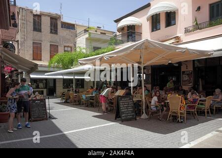Locals and tourists alike enjoy refreshments and relief from the hot sun in Petichaki Square, Rethymnon. Stock Photo