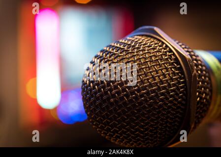 Microphone in a karaoke bar. Close up shot of a black mic with karaoke screen monitor in the background. Stock Photo