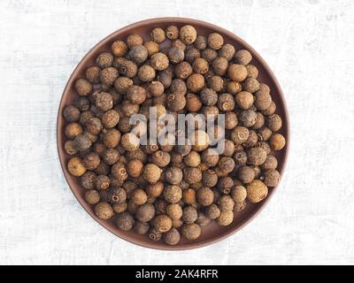 Spices and herbs help maintain good health and improve appetite, top view on white concrete background. Allspice in clay plate. Modern apothecary, nat Stock Photo