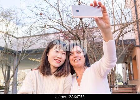 young female friends multi-ethnic taking a selfie with smartphone during an outdoor aperitif Stock Photo