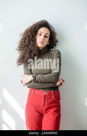 Young woman with curly hair in casual dress against white wall released Stock Photo