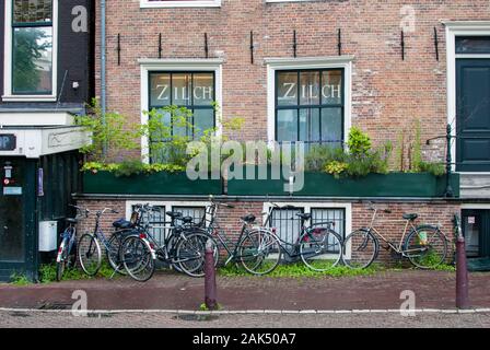 Brick wall building with many bikes parked in front of it and the sidewalk is wet of the rain Stock Photo