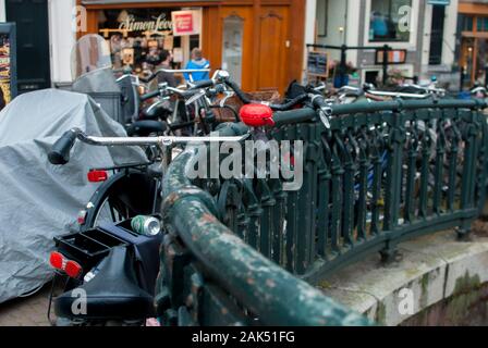 Parked bicycle along the bridge's green grid and on the back people pass through with restaurant and coffee shop Stock Photo