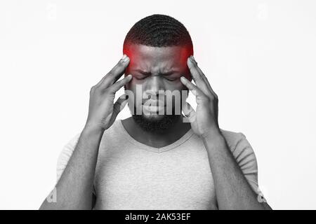 Afro man with headache touching his highlighted temples, emotional black and white photo Stock Photo