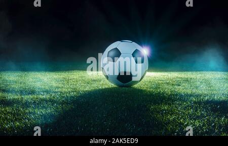 Football on an illuminated empty sports field at night backlit by bright spotlights in a low angle view with shadow, mist and copy space Stock Photo