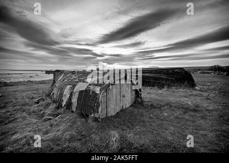 Upturned herring boats used for storage by local fishermen, Lindisfarne, Northumberland Stock Photo