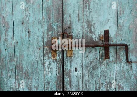 Rusty door bolt sliding latch and padlock on old weathered wooden gate with chipped blue paint. Stock Photo